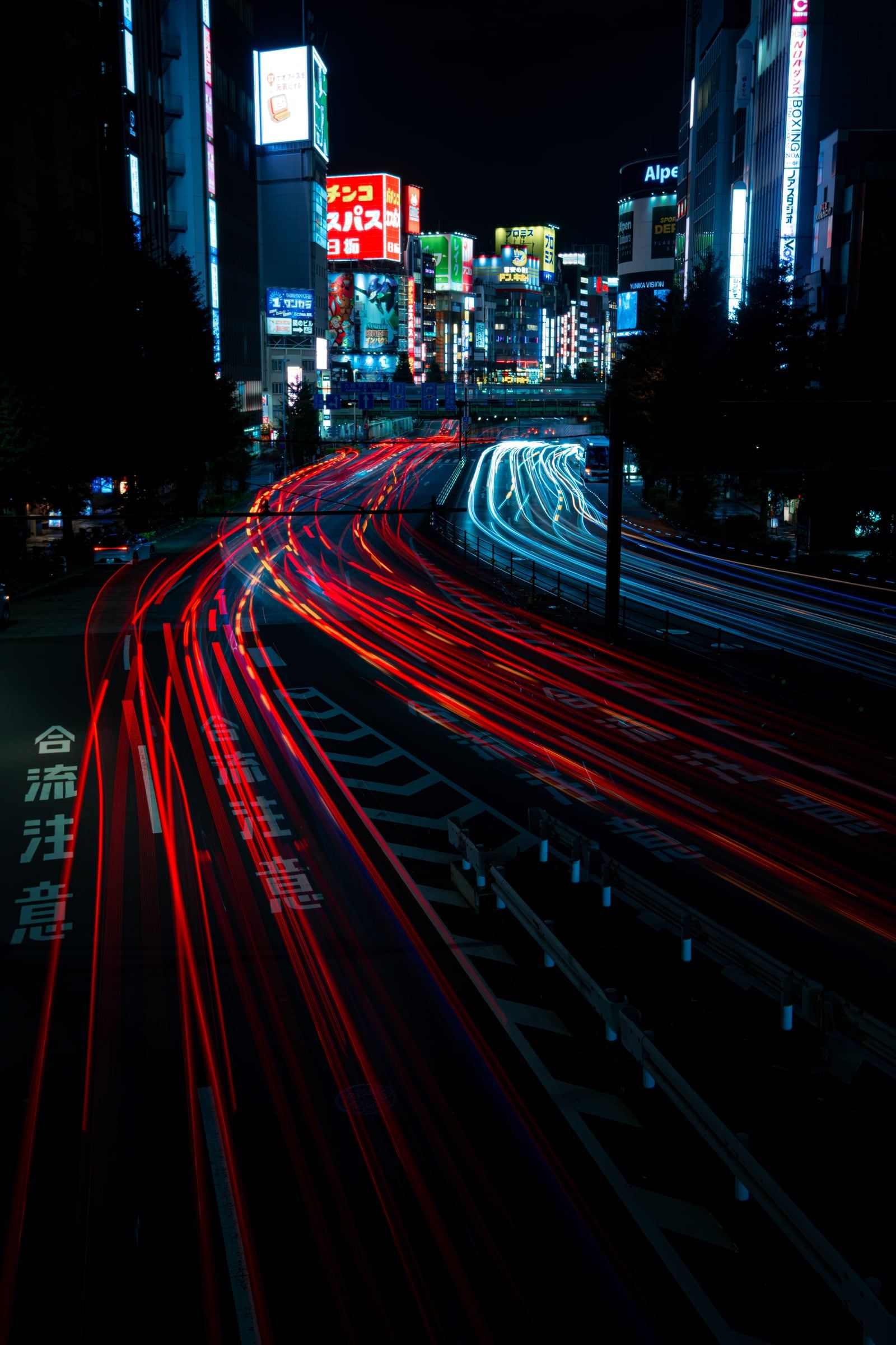 Red and white light trails flow along a neon-lit Tokyo avenue at night.