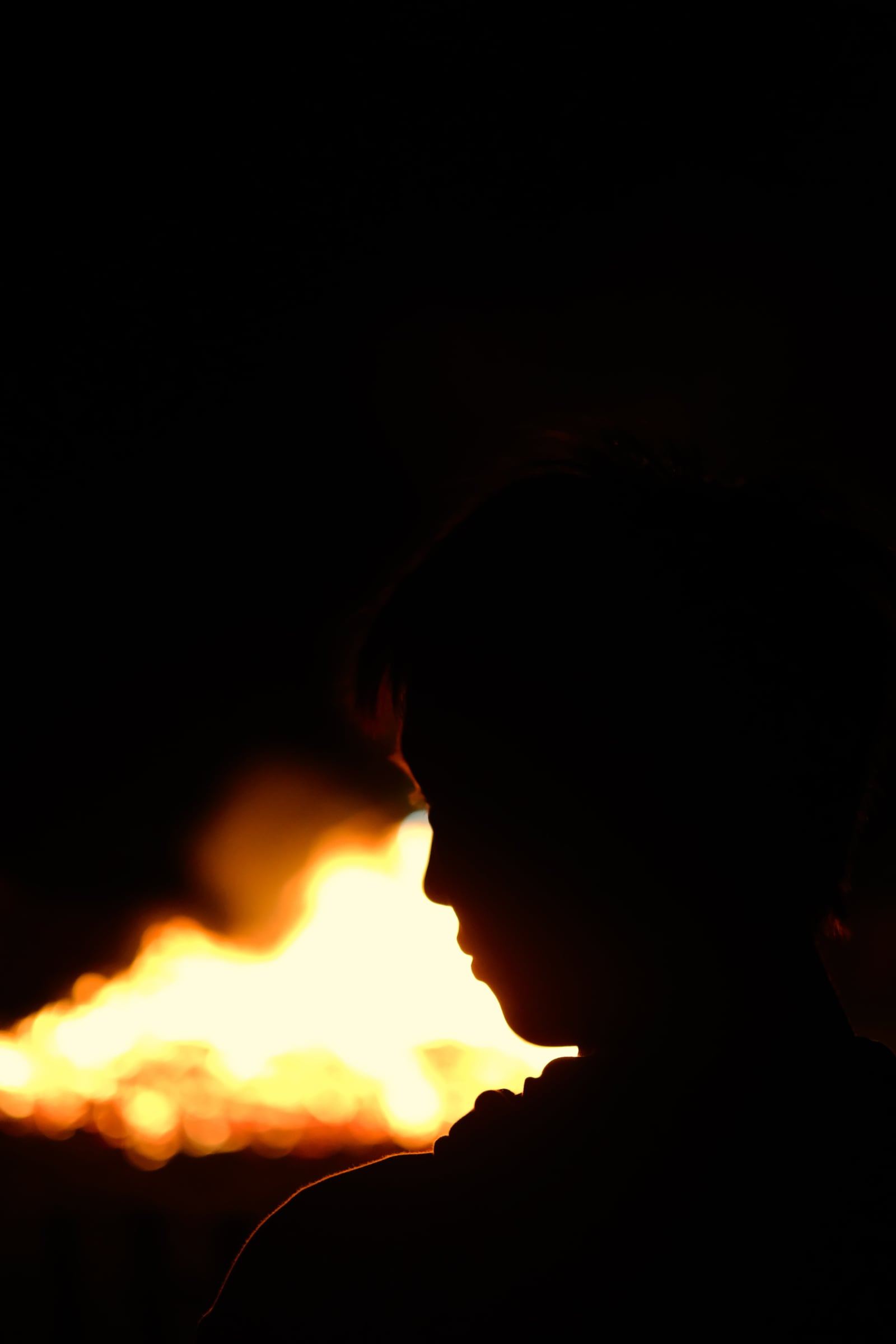 A silhouetted profile against a blurred bonfire in the dark.