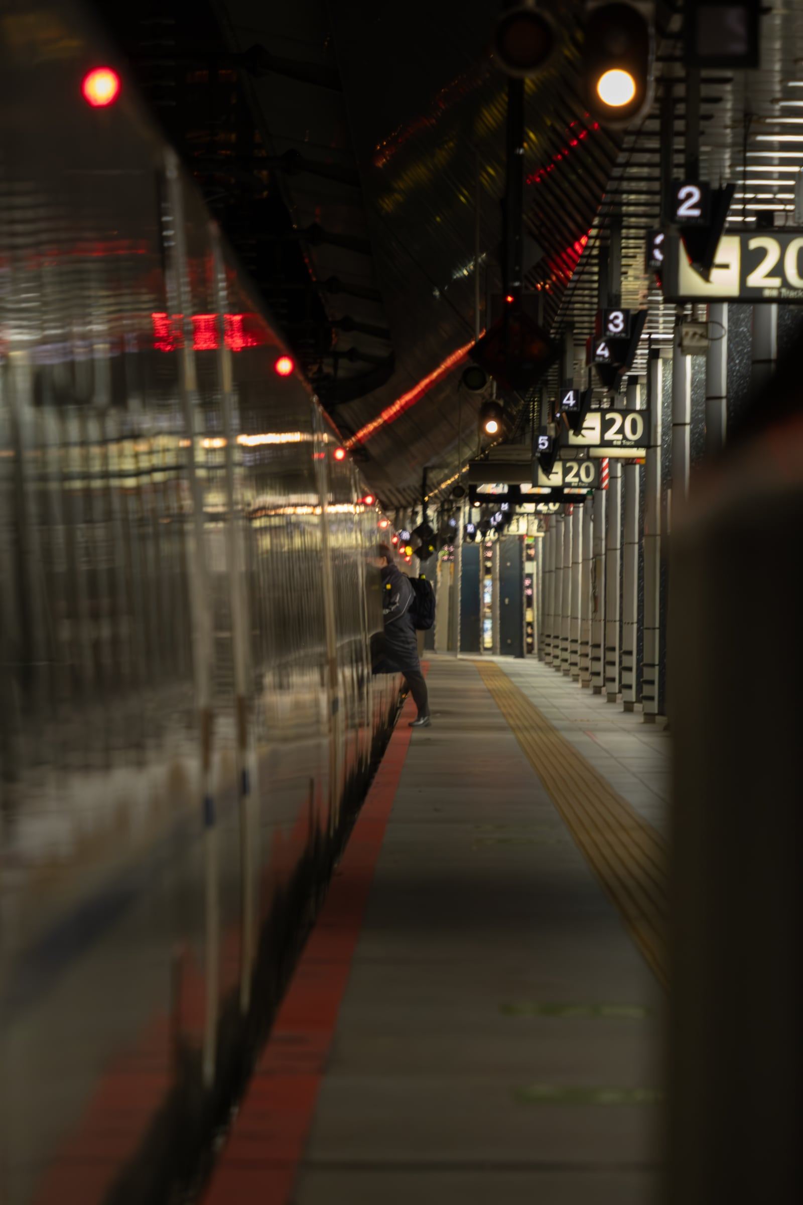 A traveller boards a train at the end of a long, dim station platform lined with car-number signs.