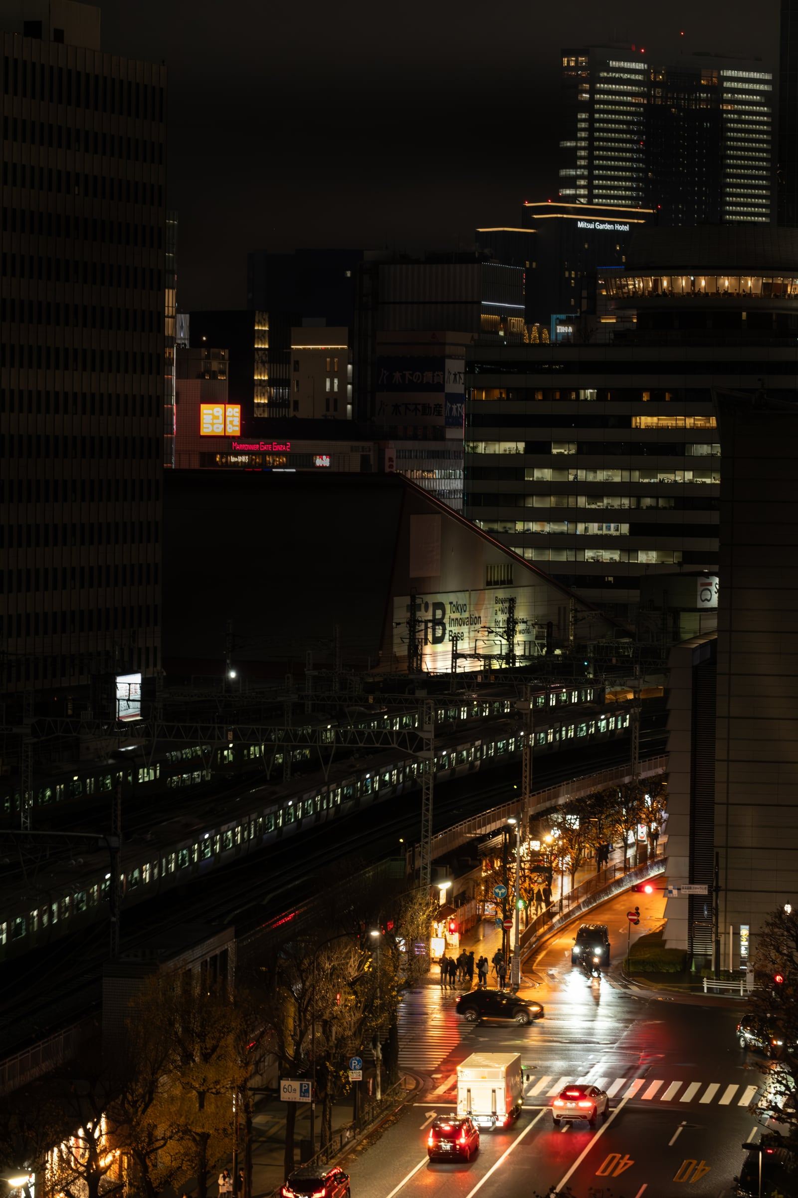 Night view over elevated rail lines and a lit street corner with taxis and pedestrians among office towers.